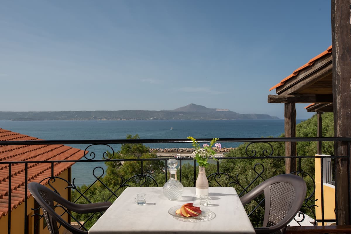 A balcony with a table set for two, overlooking a scenic view of the sea and a mountain.
