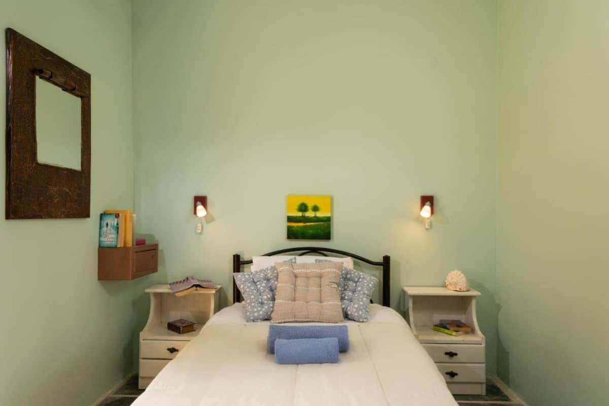 A bedroom with a bed, two bedside tables, a nightstand, a wall-mounted mirror, and a painting on the wall.