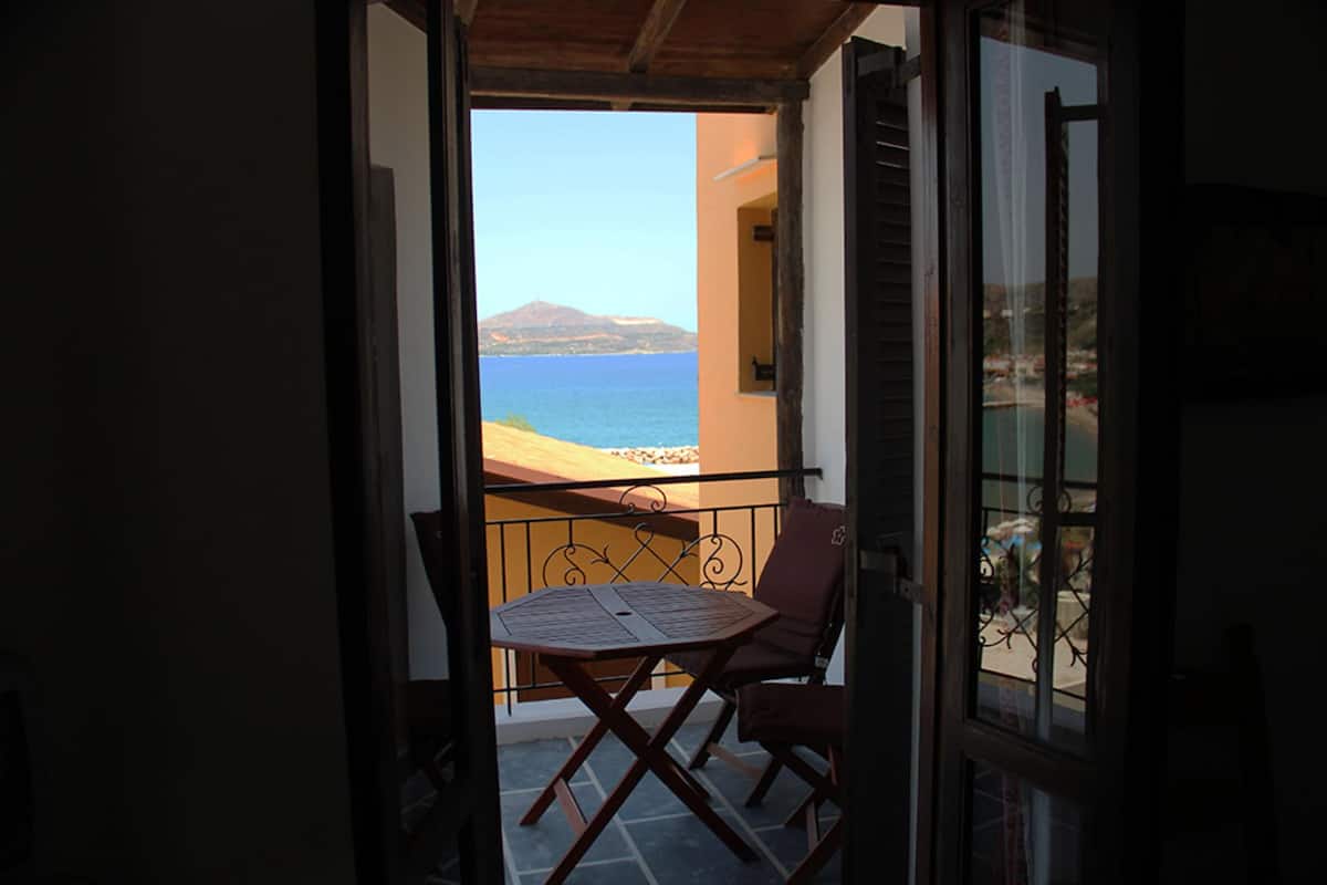 A balcony with a table and chairs, overlooking a beach and the sea.