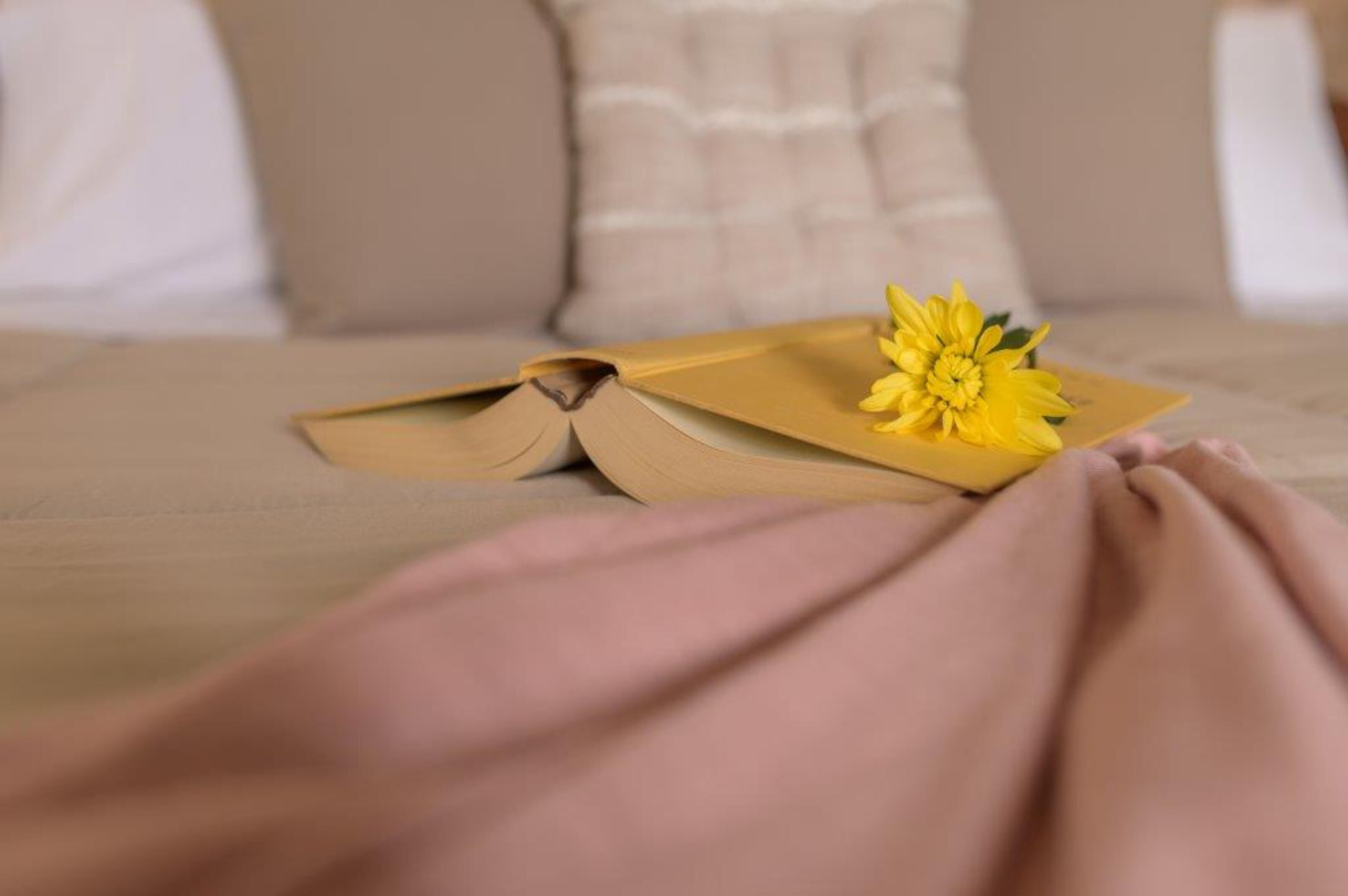 A bed with a book and a yellow flower on it.