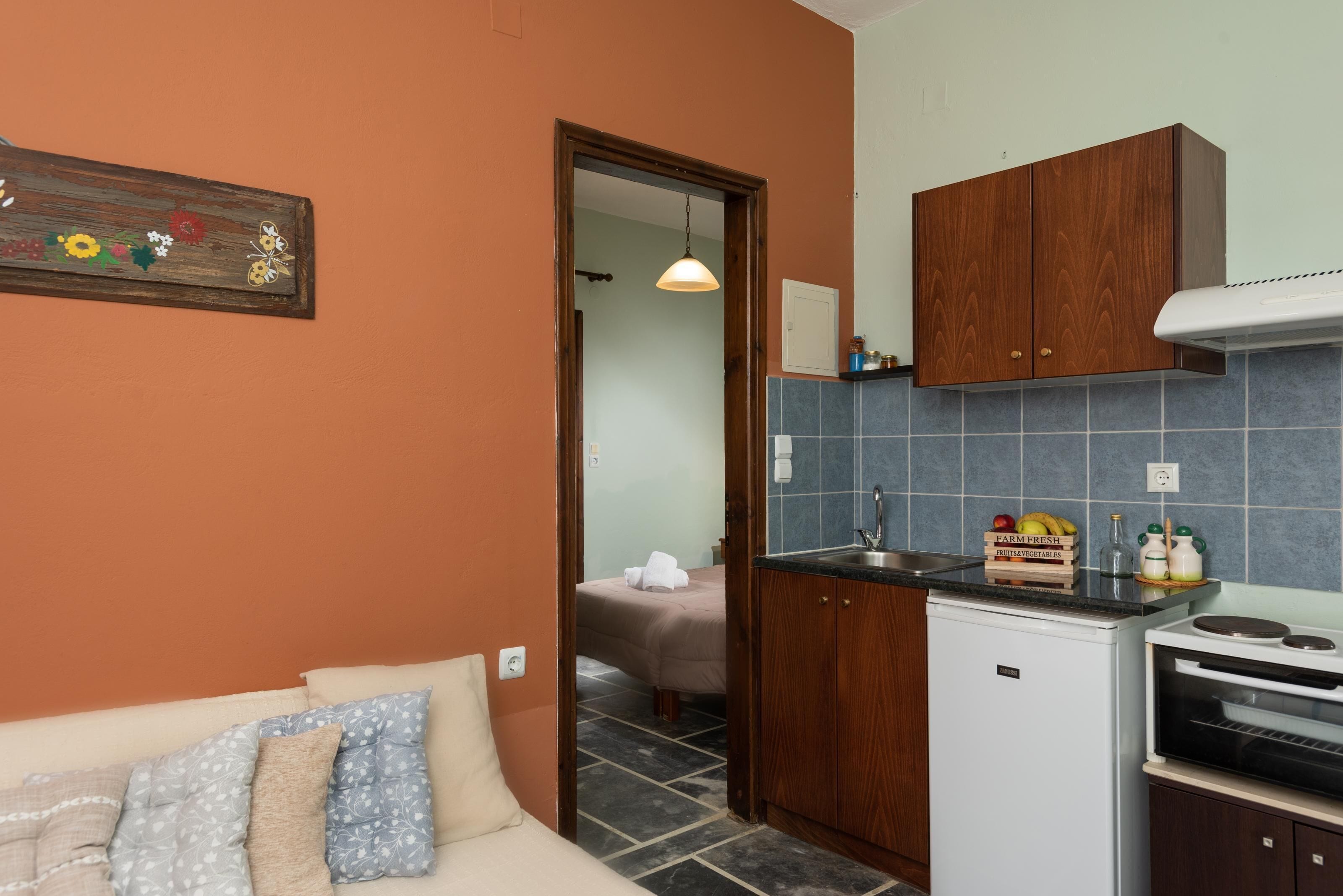 A compact kitchen with a refrigerator, oven, and wooden cabinets. A small dining area with a table and chairs is visible.
