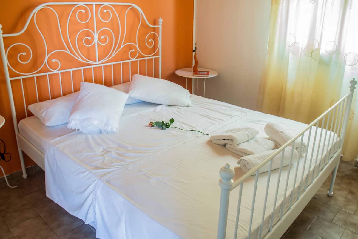 A neatly made bed with white linens and pillows, a bedside table with a book, and a small table with a vase.