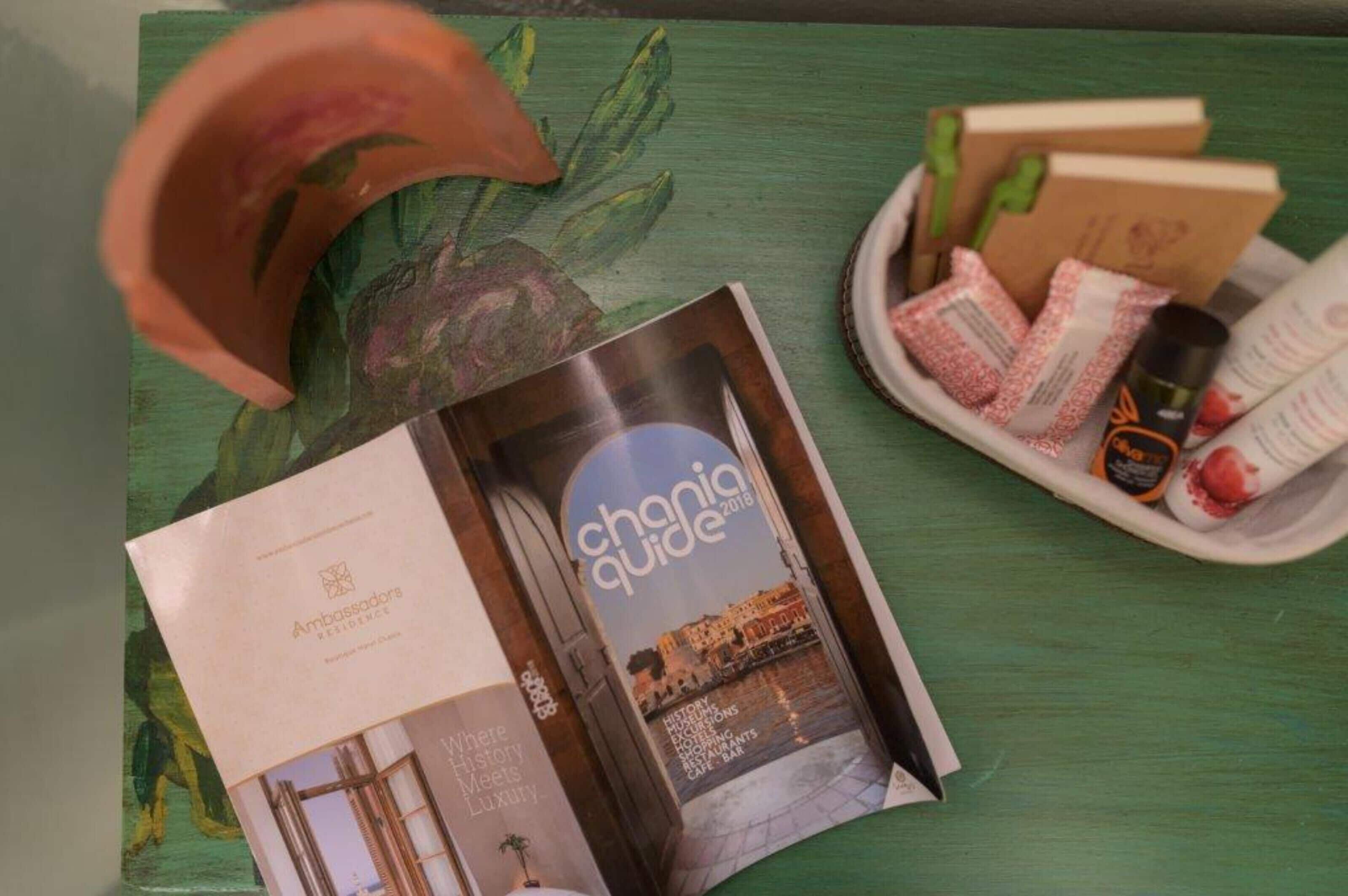 A travel guidebook titled 'Chania Guide 2018' alongside a brochure for 'Ambassadors Residence'.