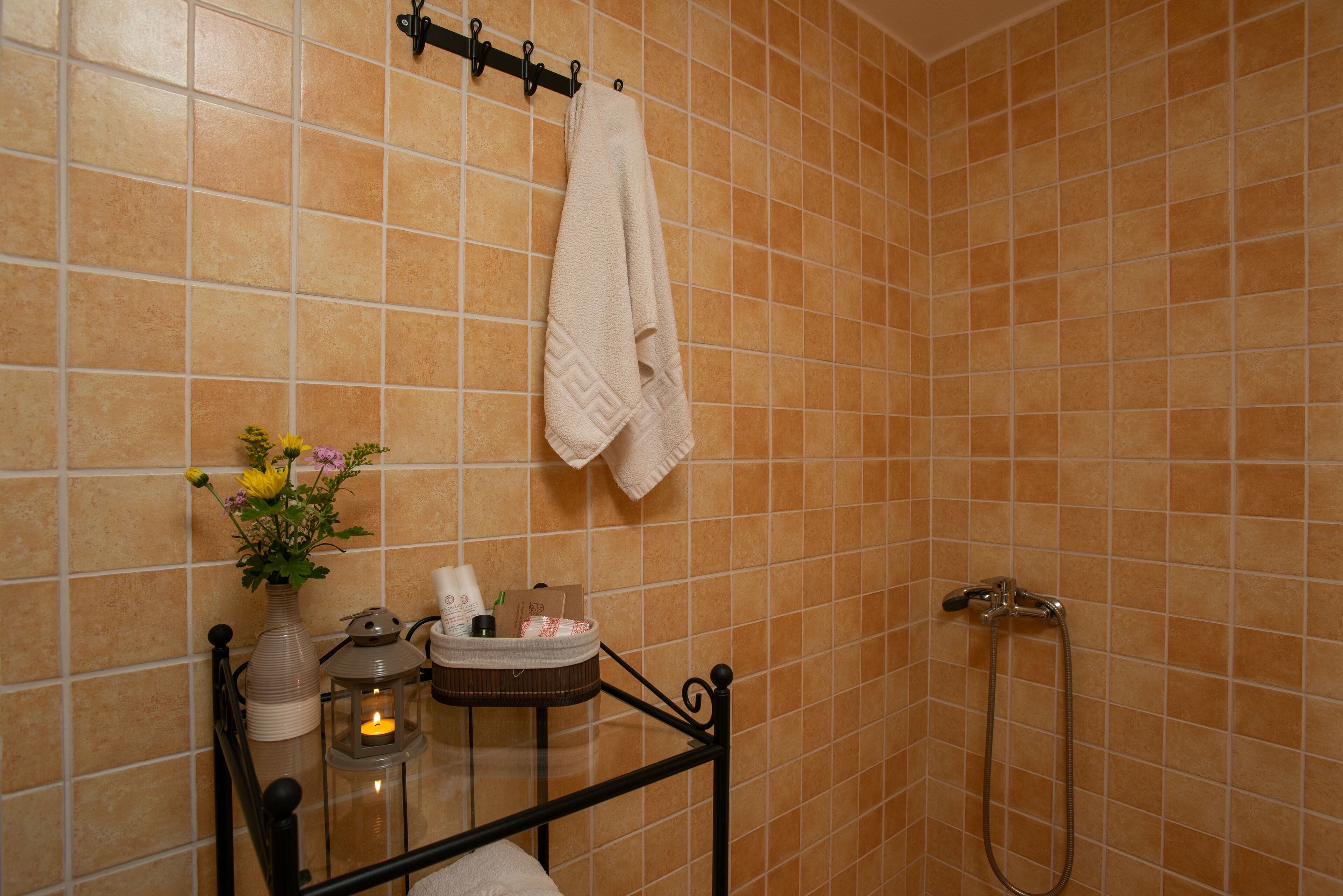A bathroom with a shower, a towel hanging on a rack, a vase with flowers, and a candle on a table.