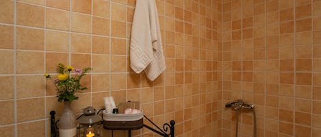 A bathroom with a shower, a towel hanging on a rack, a vase with flowers, and a candle on a table.