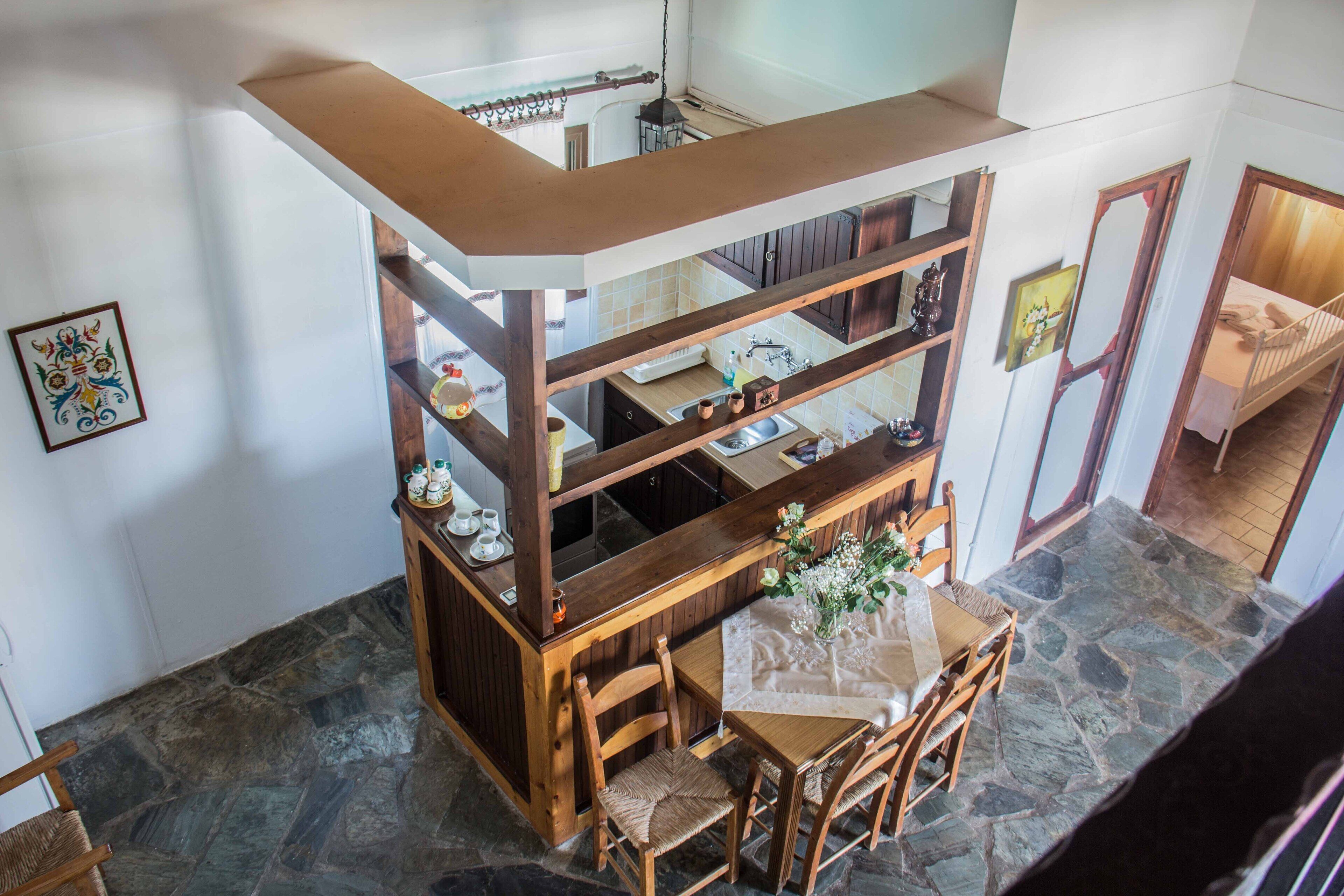 A dining area with a wooden table and chairs, a kitchen area with a sink and cabinets, and a stone floor.