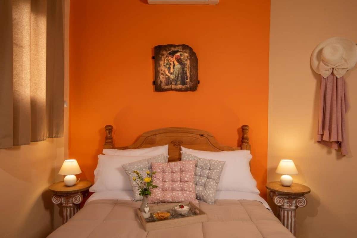 A bedroom with an orange wall, a wooden headboard, white bedding, and two bedside lamps.