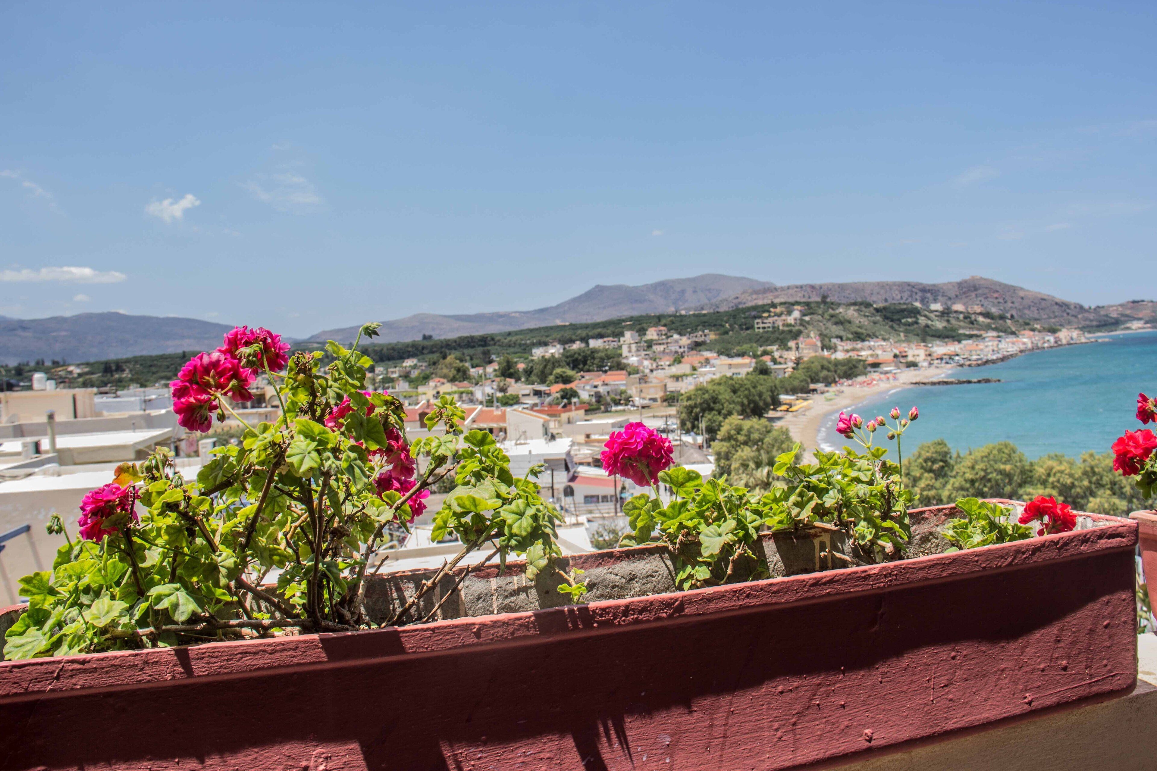 A balcony with red-painted railings overlooking a coastal town with buildings and a beach.