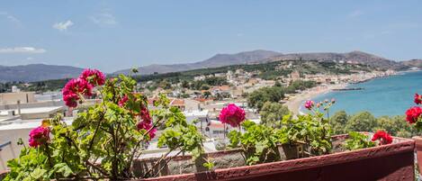 A balcony with red-painted railings overlooking a coastal town with buildings and a beach.