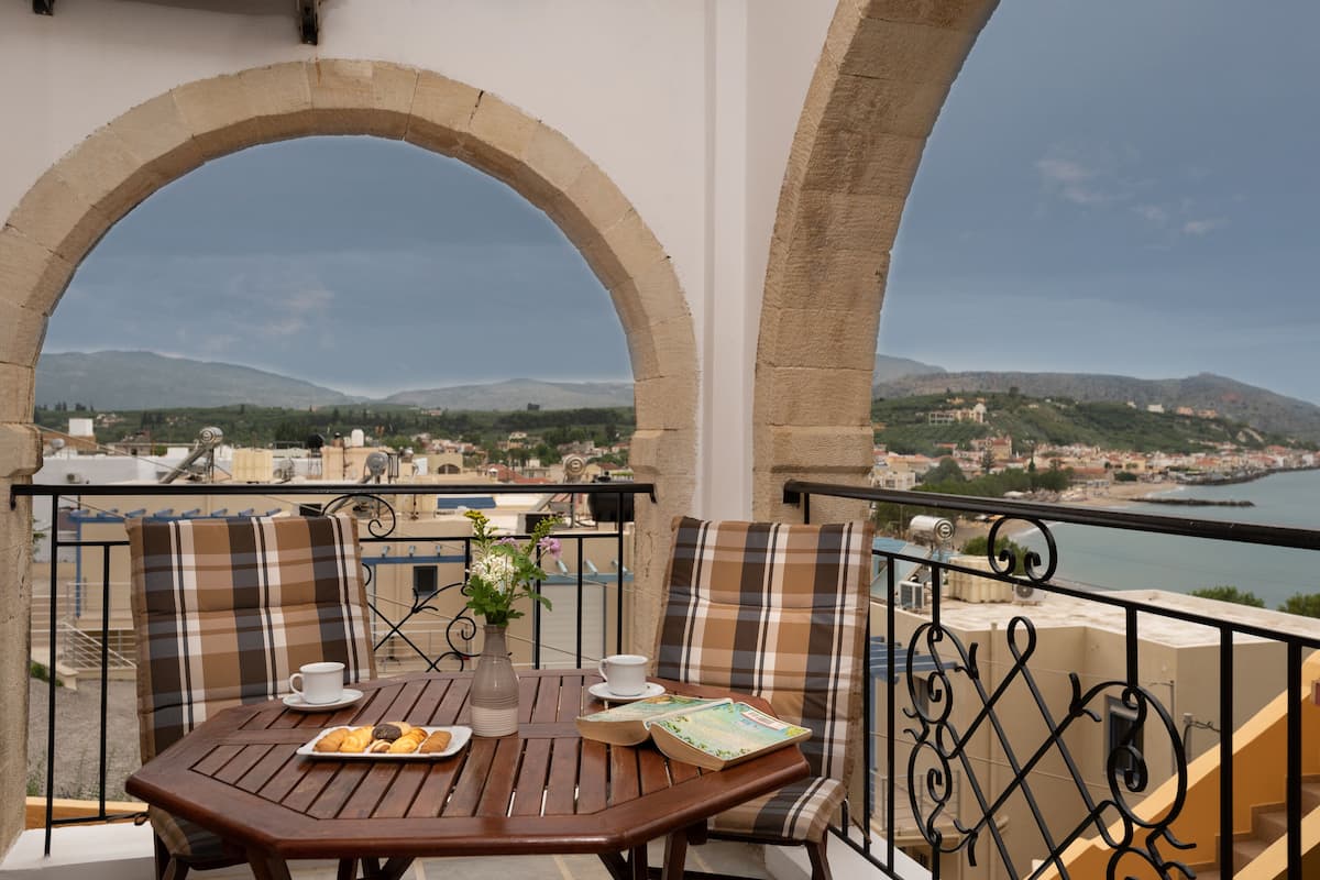A balcony with a table, chairs, and a view of a coastal town.