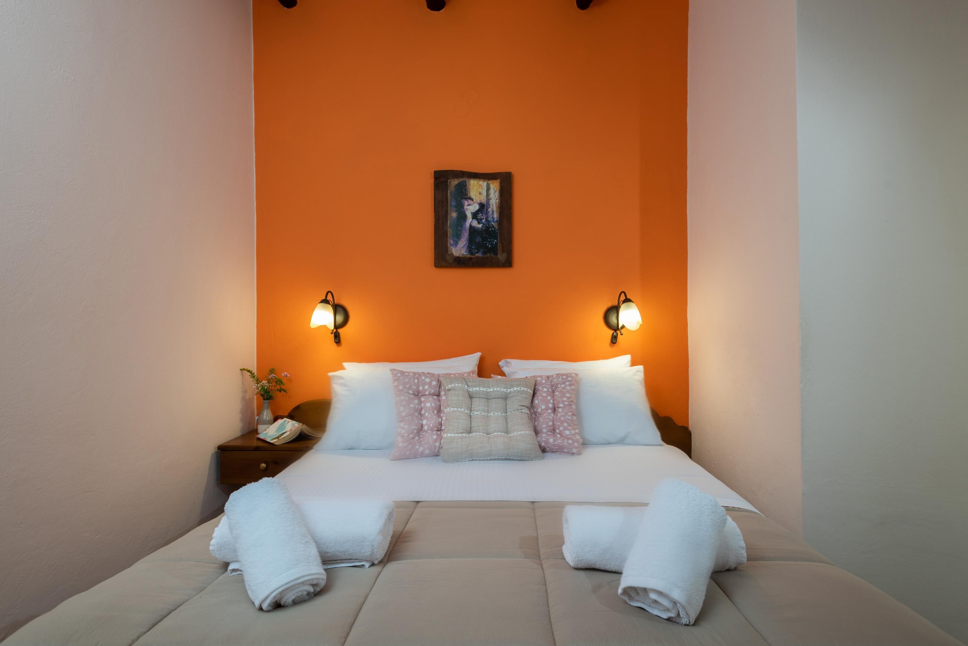 A neatly made bed with white linens, two bedside lamps, and a painting on the wall.
