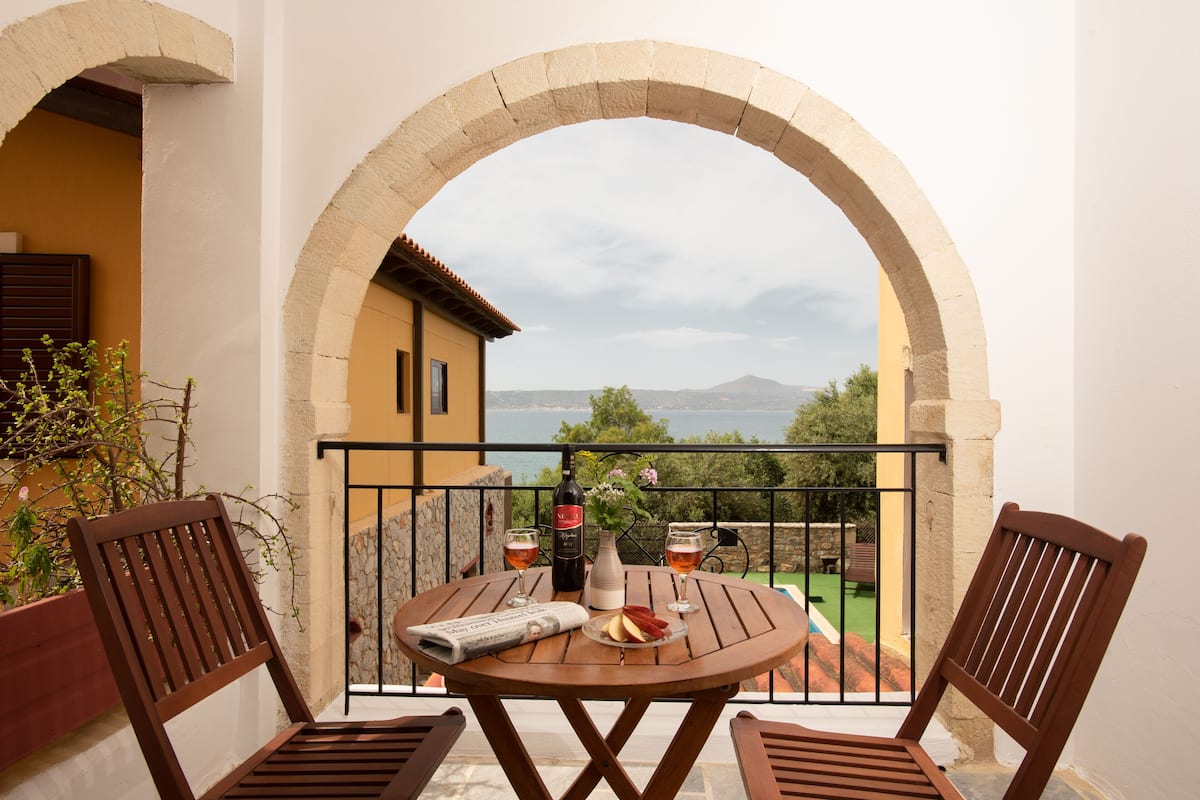A balcony with a table set for two, a bottle of wine, and a vase with flowers.