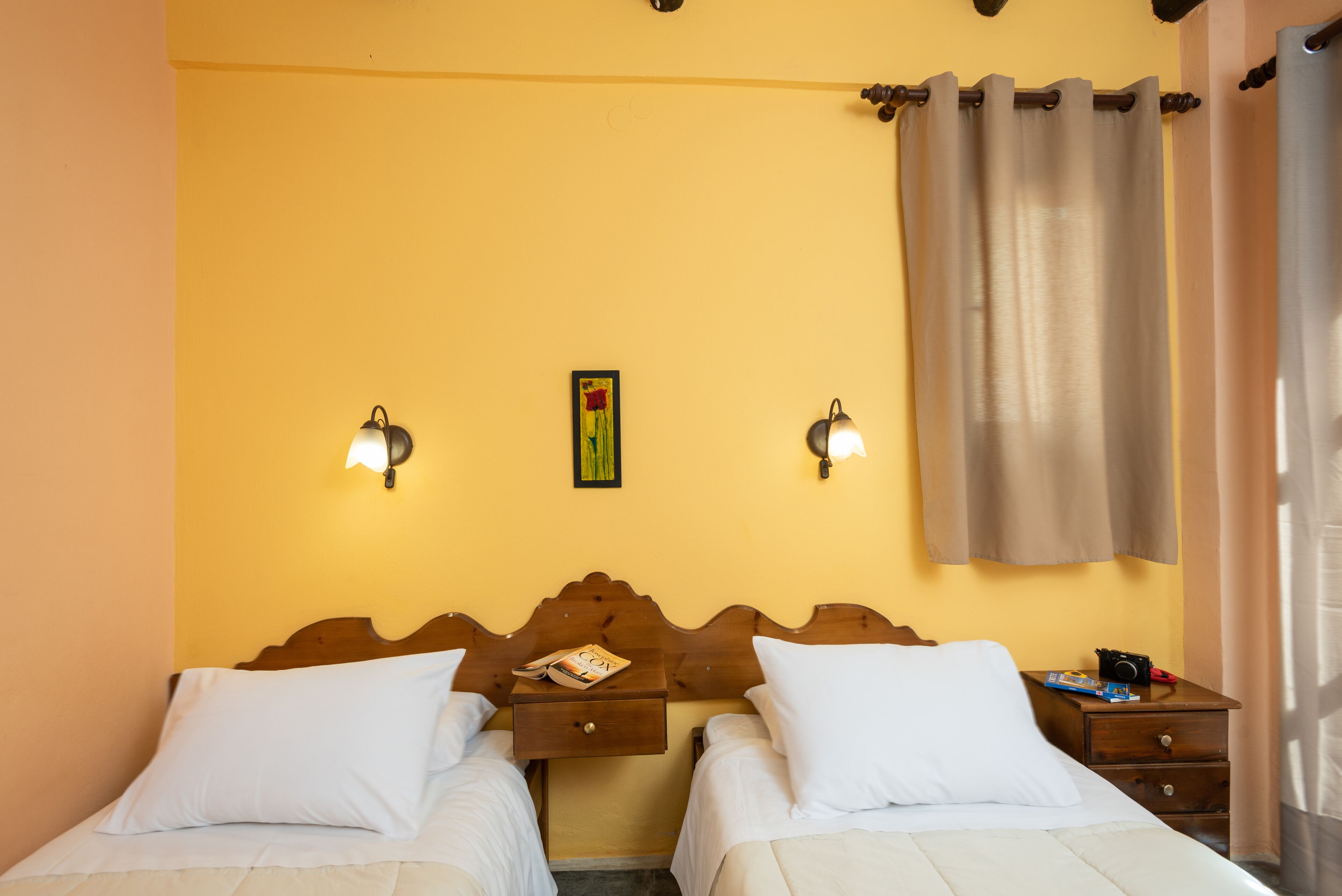 Una habitación de hotel con dos camas individuales, un cabecero de madera, mesitas de noche con lámparas y una cortina en la ventana.
