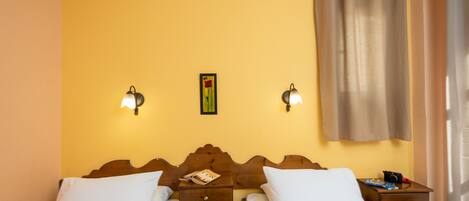 Una habitación de hotel con dos camas individuales, un cabecero de madera, mesitas de noche con lámparas y una cortina en la ventana.