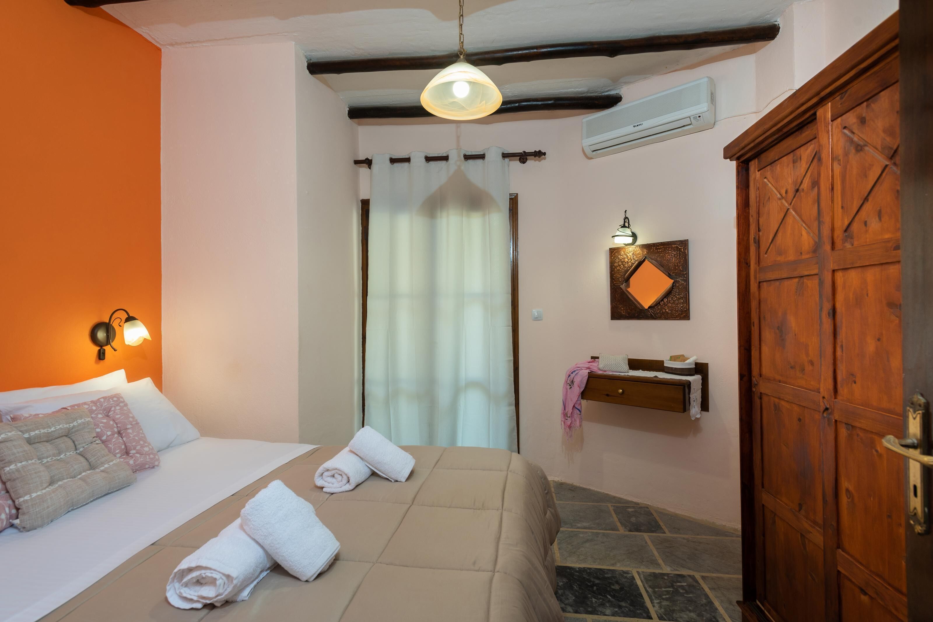 A bedroom with a bed, a wooden wardrobe, a wall-mounted shelf, and a curtain.