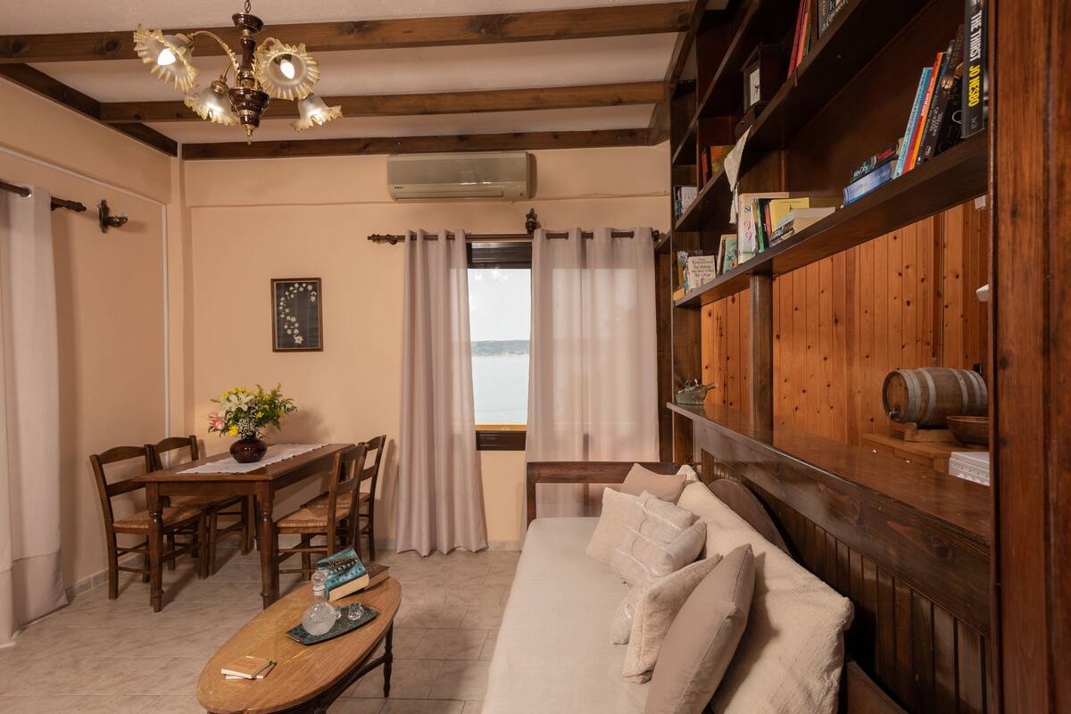 A cozy room with a wooden ceiling, a sofa, a dining table with chairs, and a bookshelf.