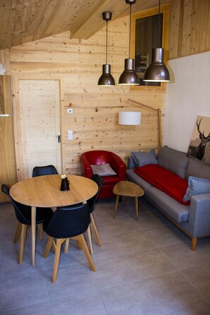Un interior de madera con una mesa redonda, sillas, un sillón rojo, un sofá gris y una pintura de un ciervo.