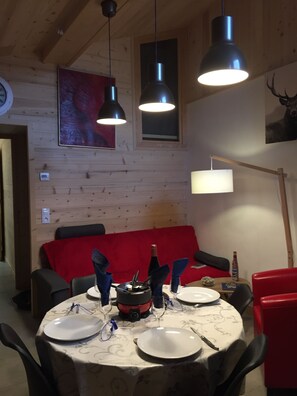 Uma sala de jantar com uma mesa redonda posta para quatro pessoas, um sofá vermelho e uma parede de madeira com um quadro.