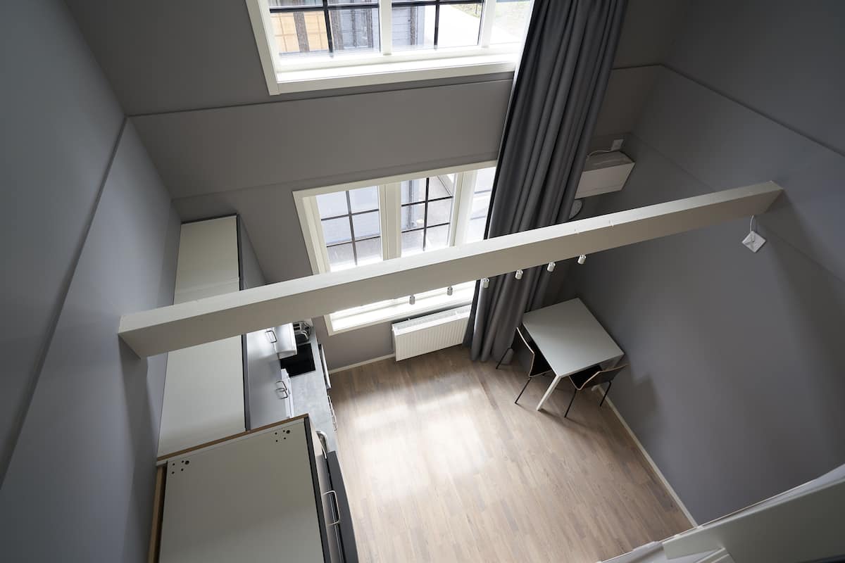 Una stanza con soffitto alto e vista dalla finestra, un termosifone bianco e un tavolino.