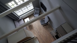 A modern interior with a high ceiling, a seating area with sofas, a flat-screen TV, and a kitchen area.