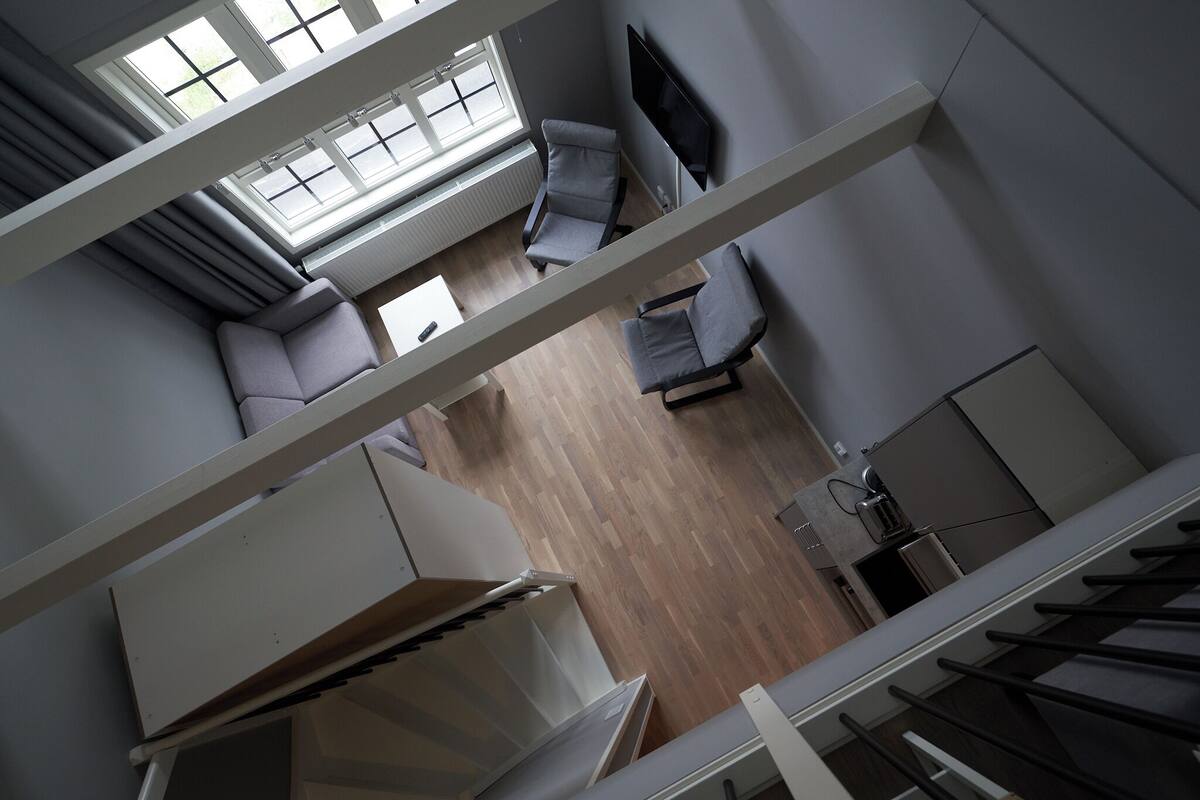 Un interno moderno con soffitto alto, una zona salotto con divani, una TV a schermo piatto e un angolo cucina.
