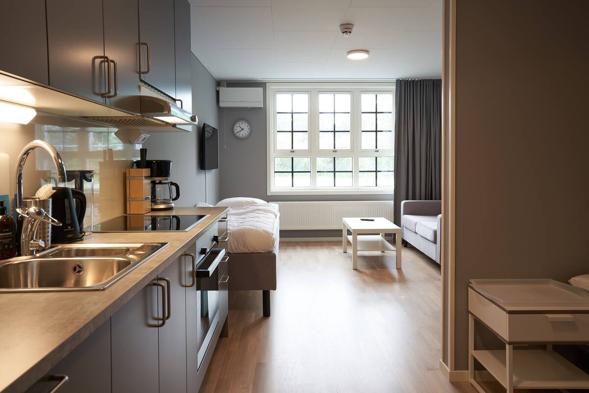 Una cucina moderna con lavello, piano cottura e macchina da caffè, una zona pranzo con tavolo e sedie e un soggiorno con divano e finestra con tende.