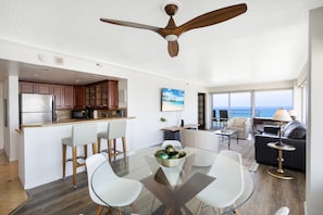 A modern kitchen with wooden cabinets, a stainless steel refrigerator, and a dining area with a glass table and white chairs.