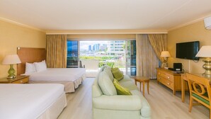 Ein Hotelzimmer mit zwei Betten, einem Sofa, einem Fernseher und einem Balkon mit Blick auf die Stadt.