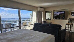 Et hotelværelse med en stor seng, en sofa, et fjernsyn og en balkon med udsigt over havet og både.
