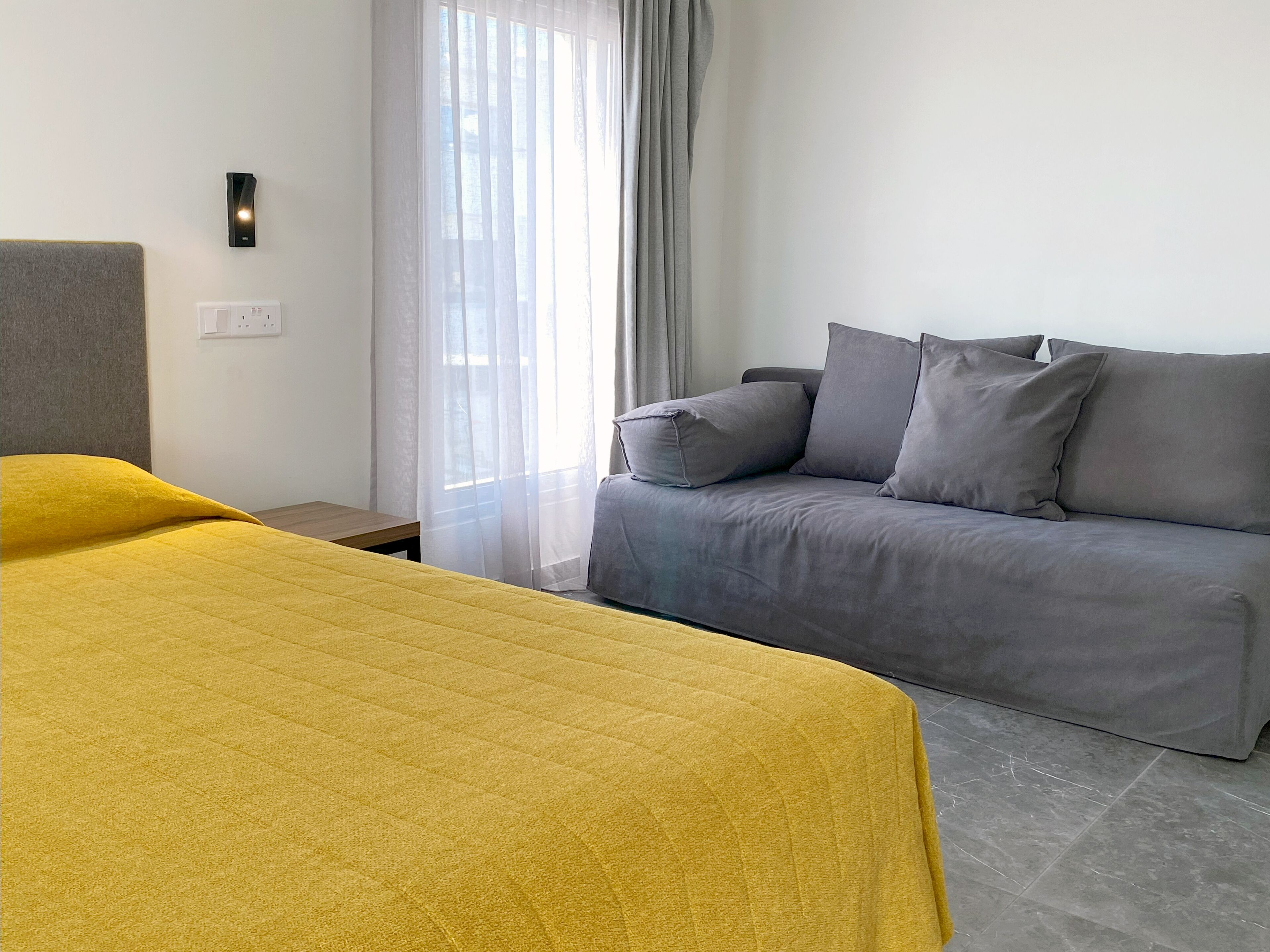 Een moderne hotelkamer met een bed, een slaapbank en een raam met gordijnen.