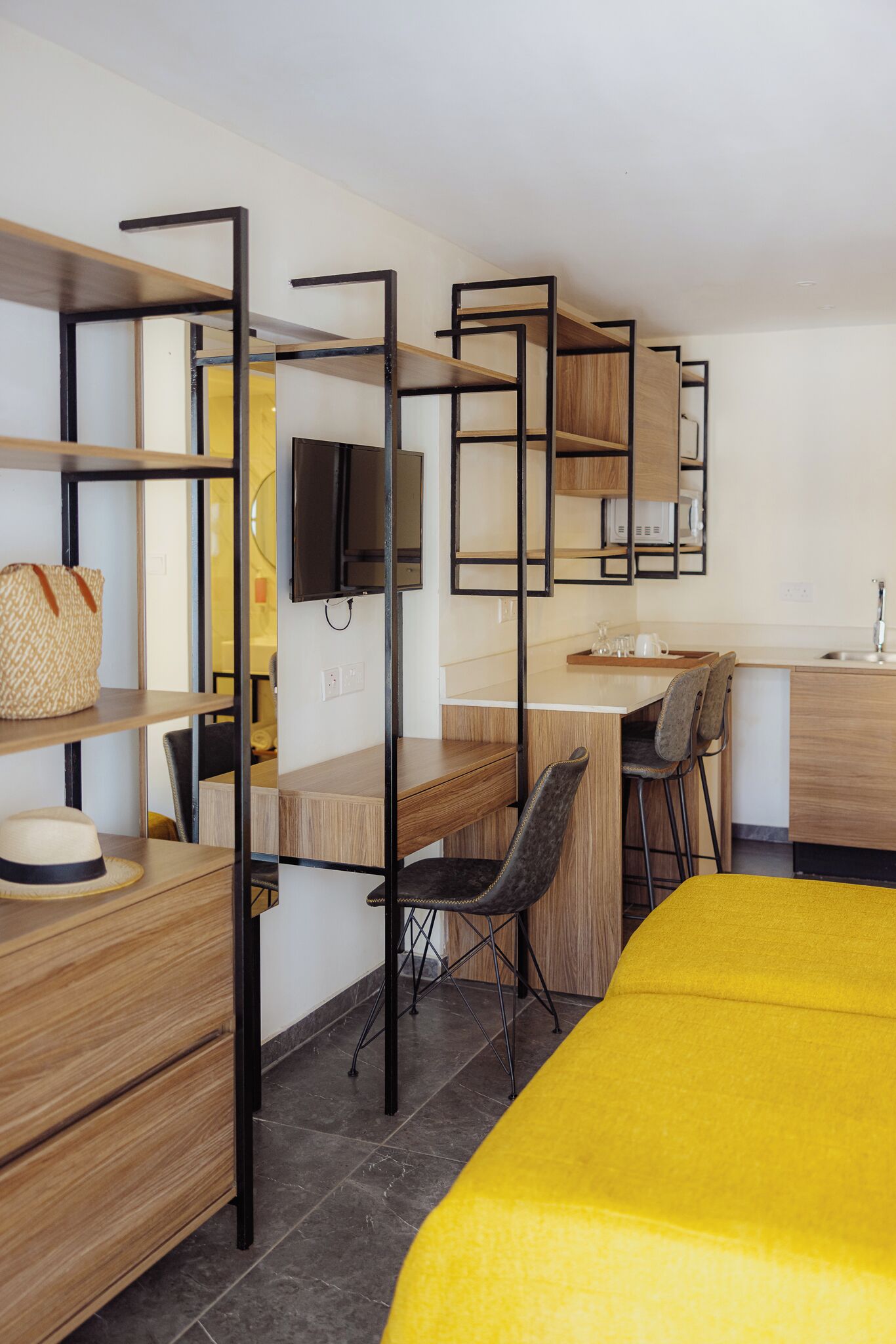 Una habitación de hotel compacta con cama, escritorio, silla, televisión y kitchenette.