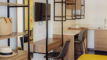 Una habitación de hotel compacta con cama, escritorio, silla, televisión y kitchenette.