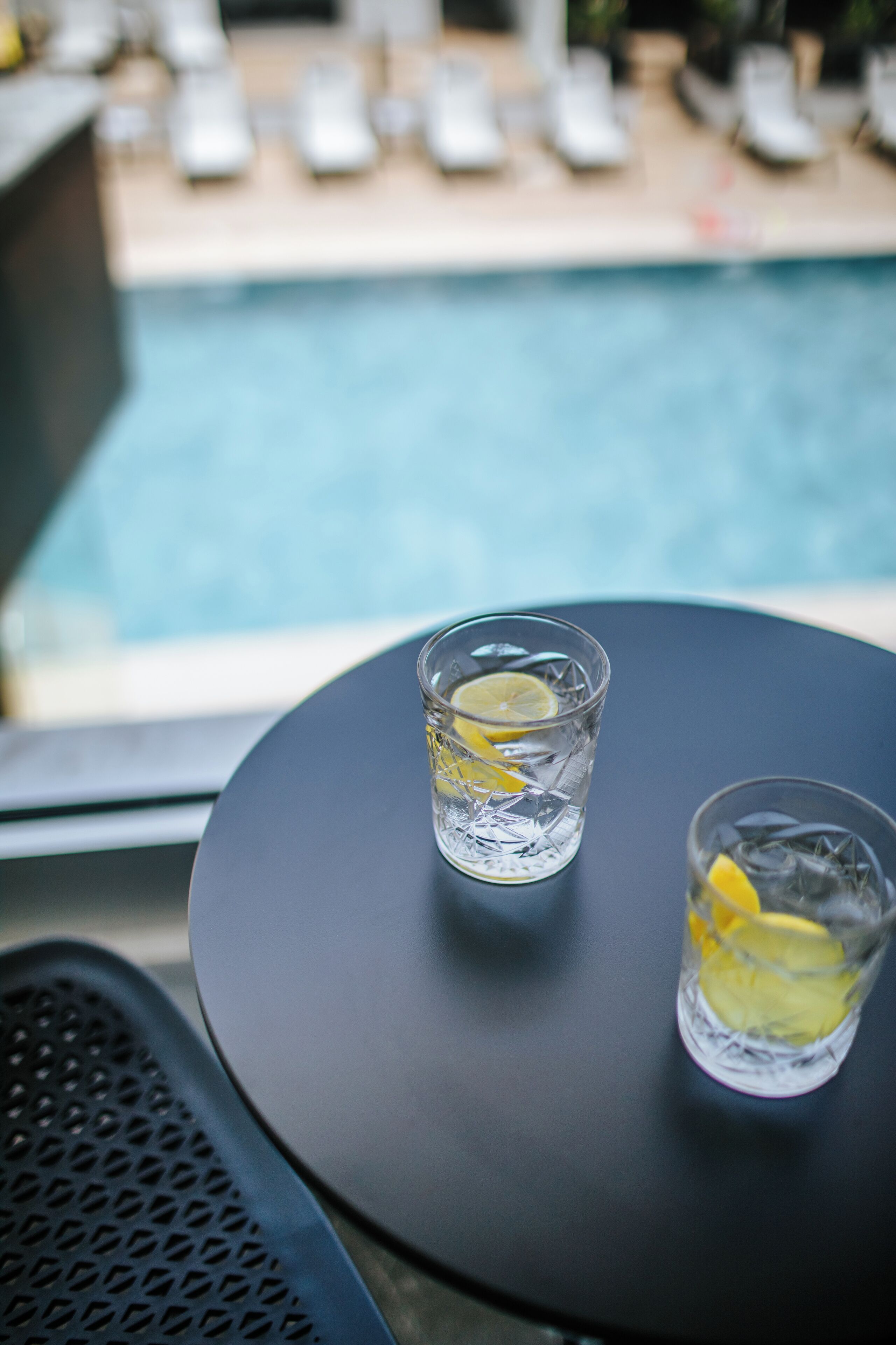 Due bicchieri d'acqua con fettine di limone su un tavolo rotondo vicino a una piscina.