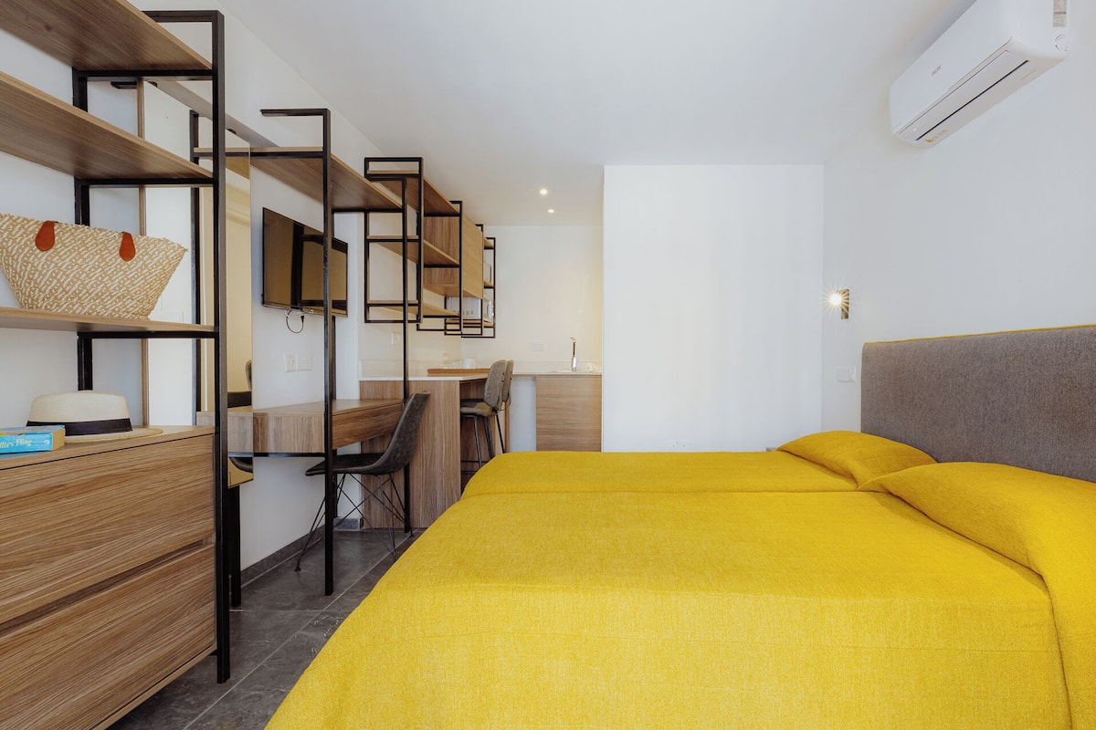 Une chambre moderne avec un lit, un bureau et une chaise. On y trouve une étagère avec un panier et un chapeau.