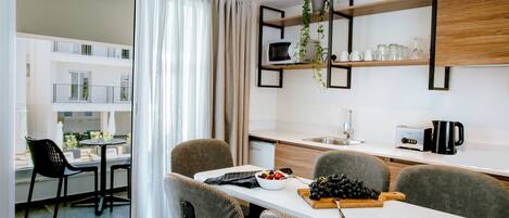 A modern kitchen with a dining area, featuring a white table, grey upholstered chairs, and a view of the balcony.