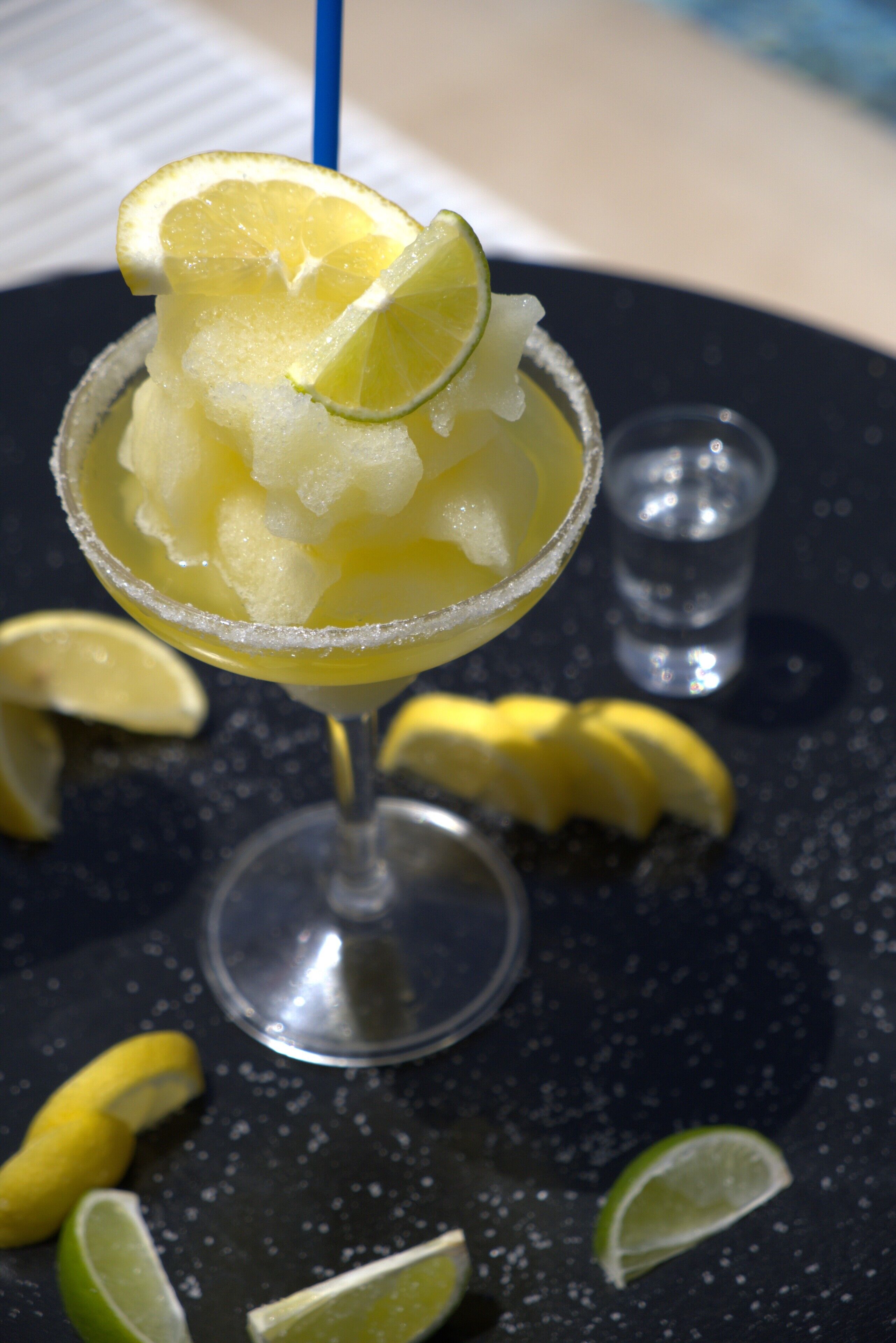 A cocktail with ice and a lime slice in a salt-rimmed glass, with a blue straw.