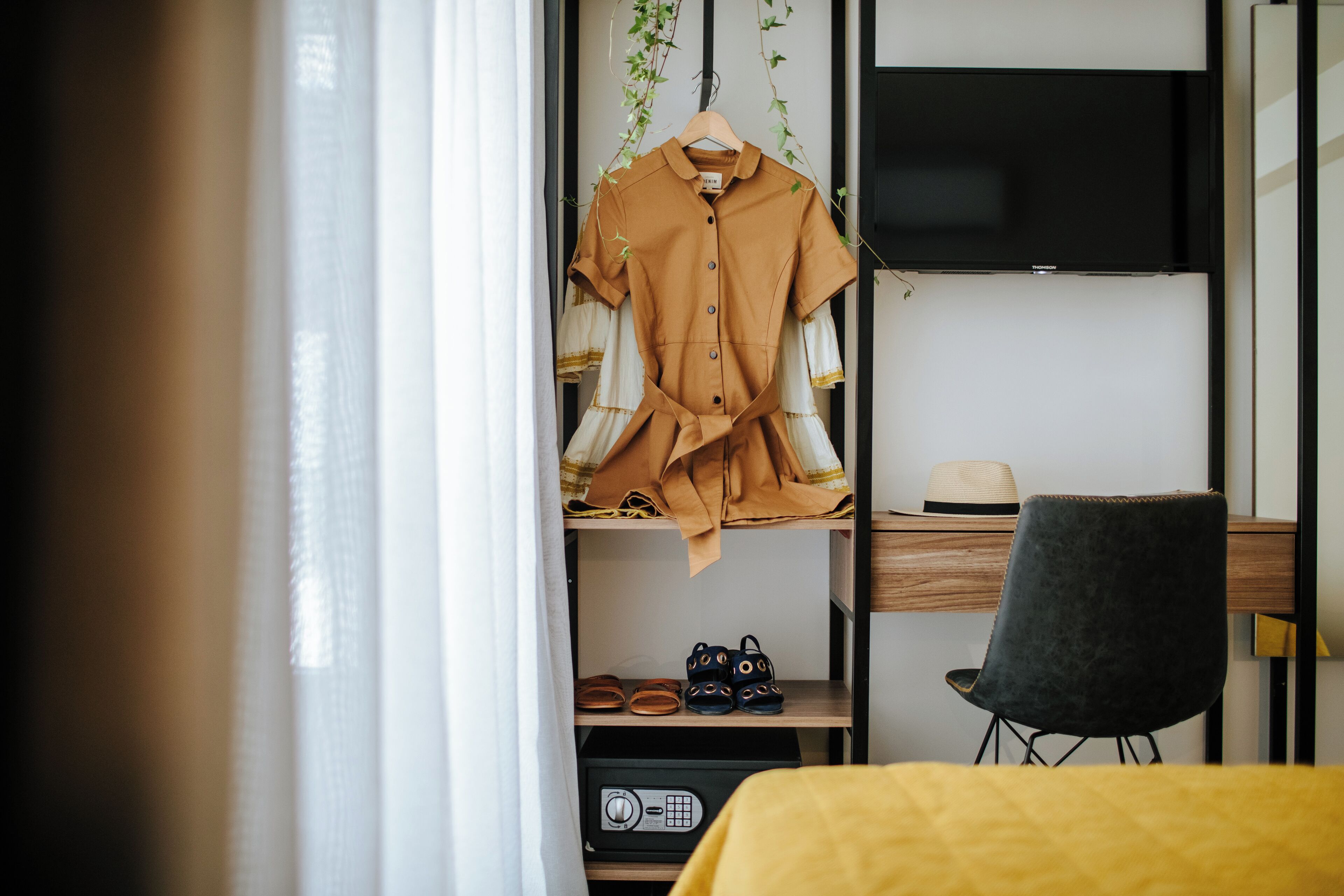 Un dormitorio ordenado con cama, escritorio, silla y armario con ropa y zapatos colgados.
