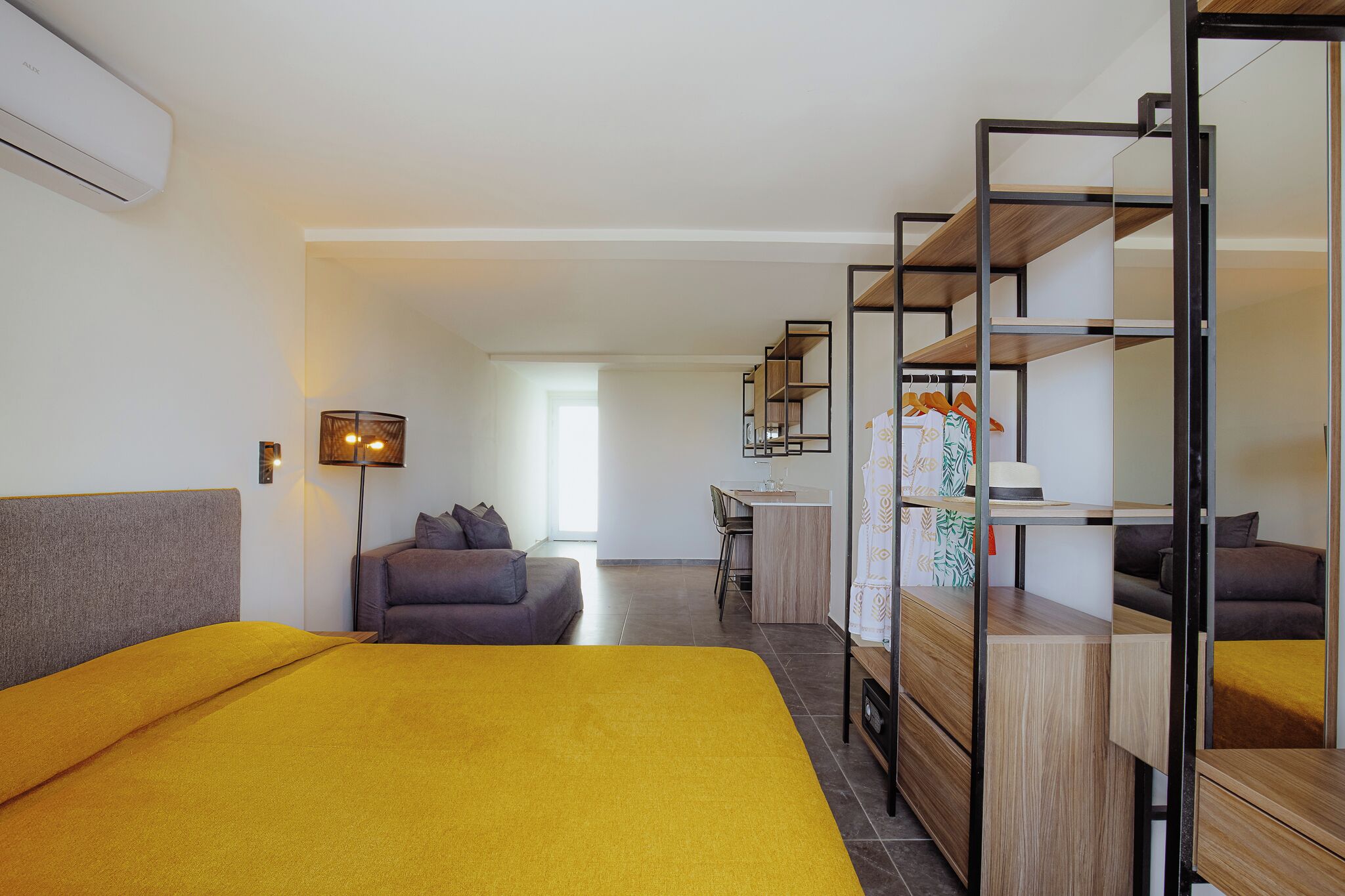 A modern hotel room with a bed, a desk, a sofa, and a wardrobe with mirrors.