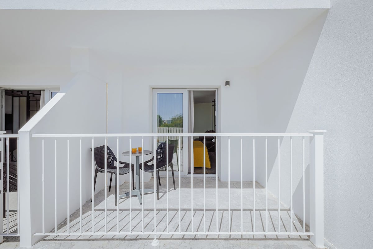 Un balcon avec une balustrade blanche, deux chaises, une petite table et une nappe jaune.