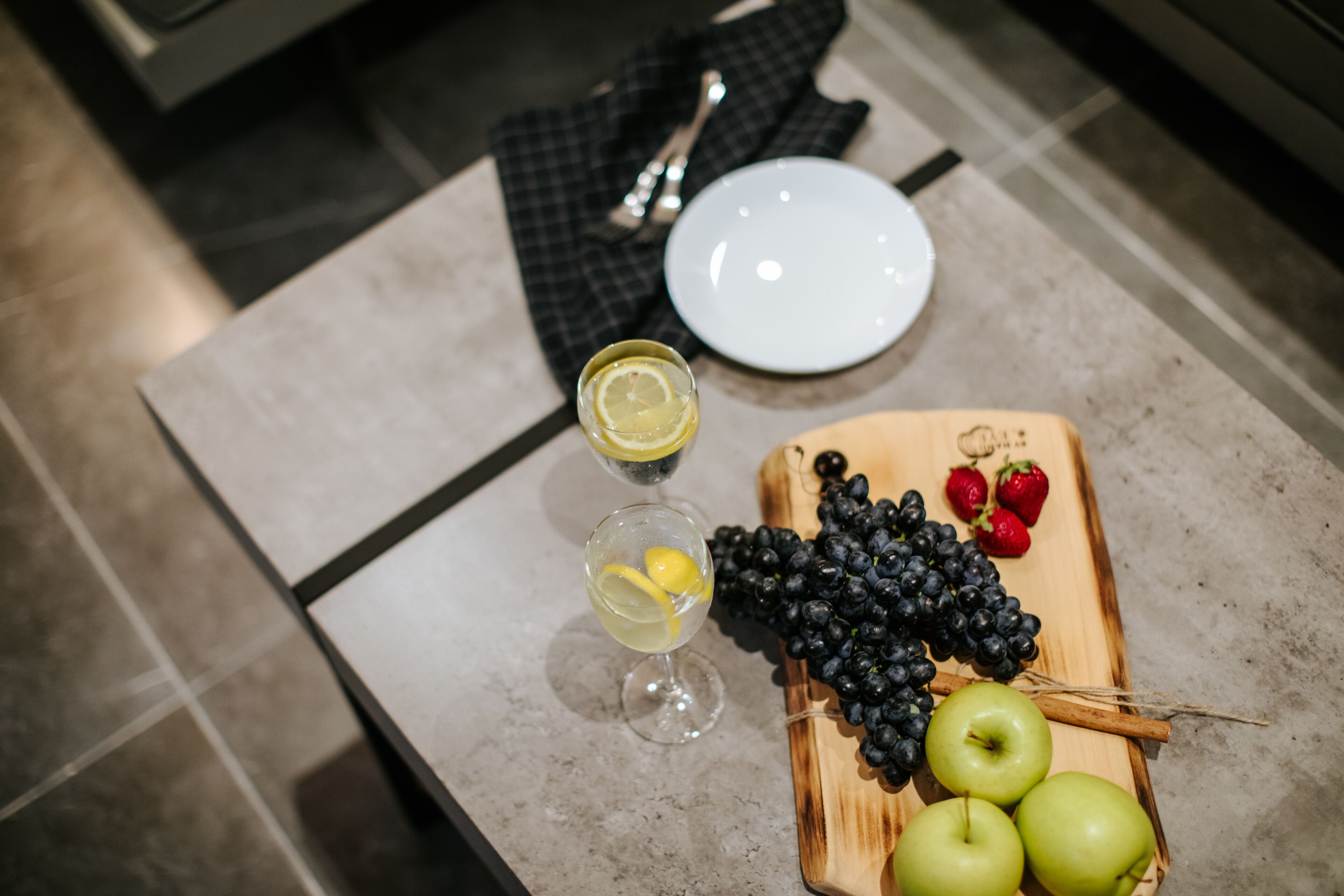 A table with a plate, a glass of drink, and a wooden board with fruits and a lemon wedge.