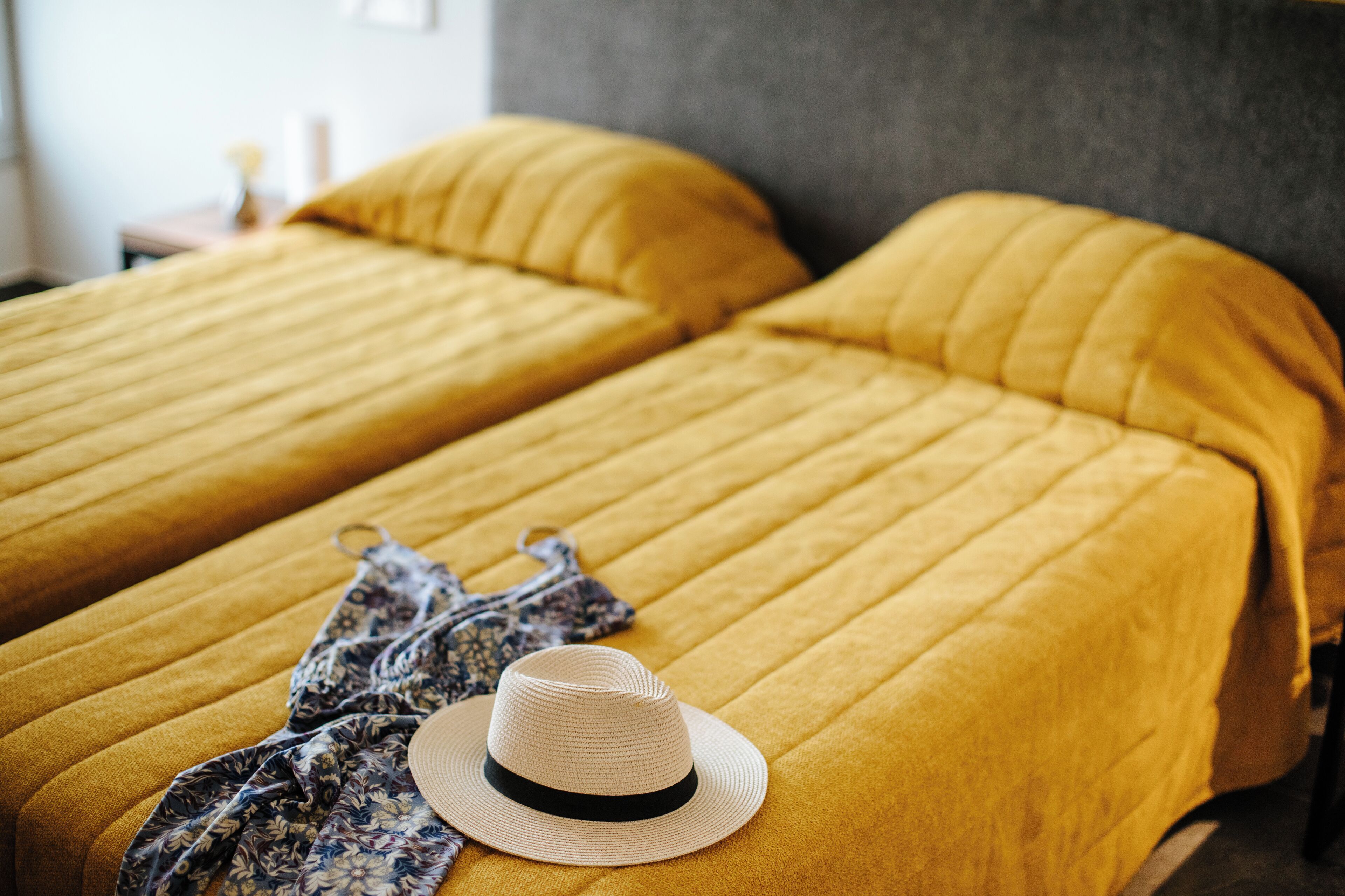 Una cama con una colcha amarilla y un sombrero encima.