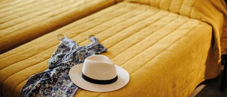 Una cama con una colcha amarilla y un sombrero encima.