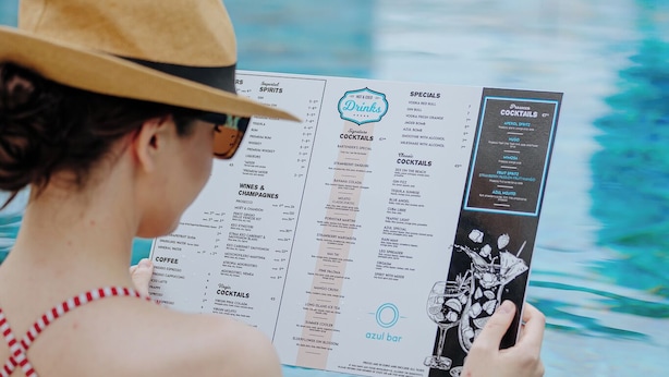 Une personne est assise au bord d’une piscine et lit un menu.