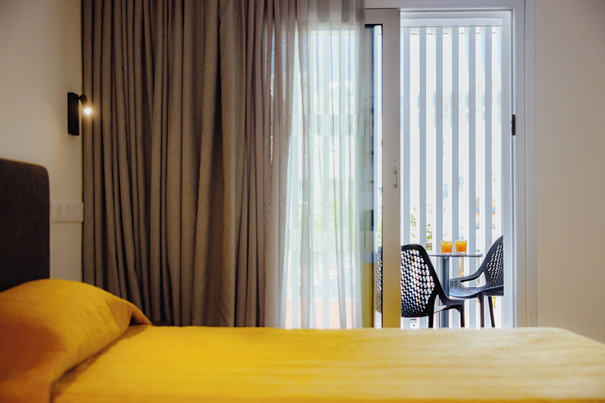 A hotel room with a bed, curtains, a sliding glass door leading to an outdoor seating area with chairs and a table.