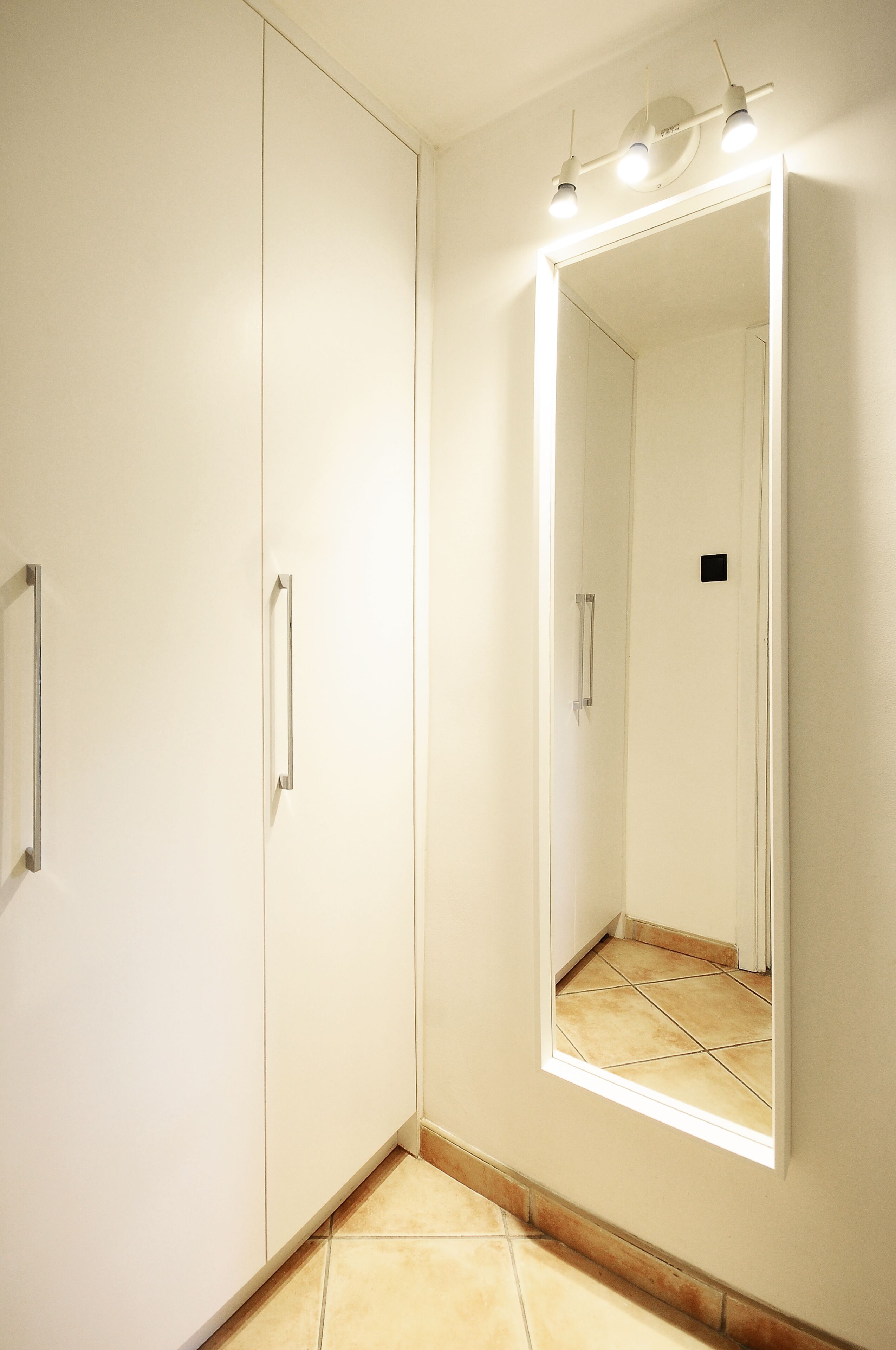 Ein Zimmer mit einem großen Spiegel, einem weißen Kleiderschrank und einem kleinen Fenster.