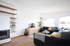 Uma sala de estar moderna com lareira, sofá preto, prateleiras de madeira e uma janela grande.