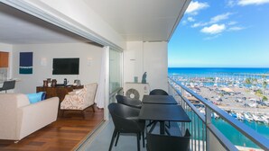 Un balcon avec vue sur l’océan, un coin repas avec des chaises et une table, et un salon avec un canapé et un téléviseur.
