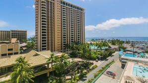 A high-rise hotel with multiple balconies, a swimming pool, and a view of the ocean.