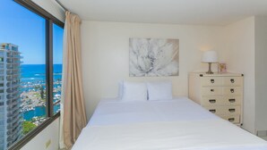 Et hotelværelse med en seng, et kommode, et maleri og udsigt til havet og bygninger.