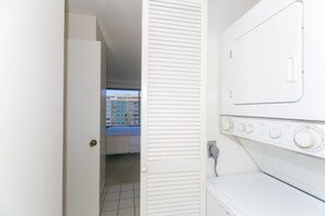 Un lavadero con lavadora y secadora, una puerta que da a un balcón con vistas a edificios.